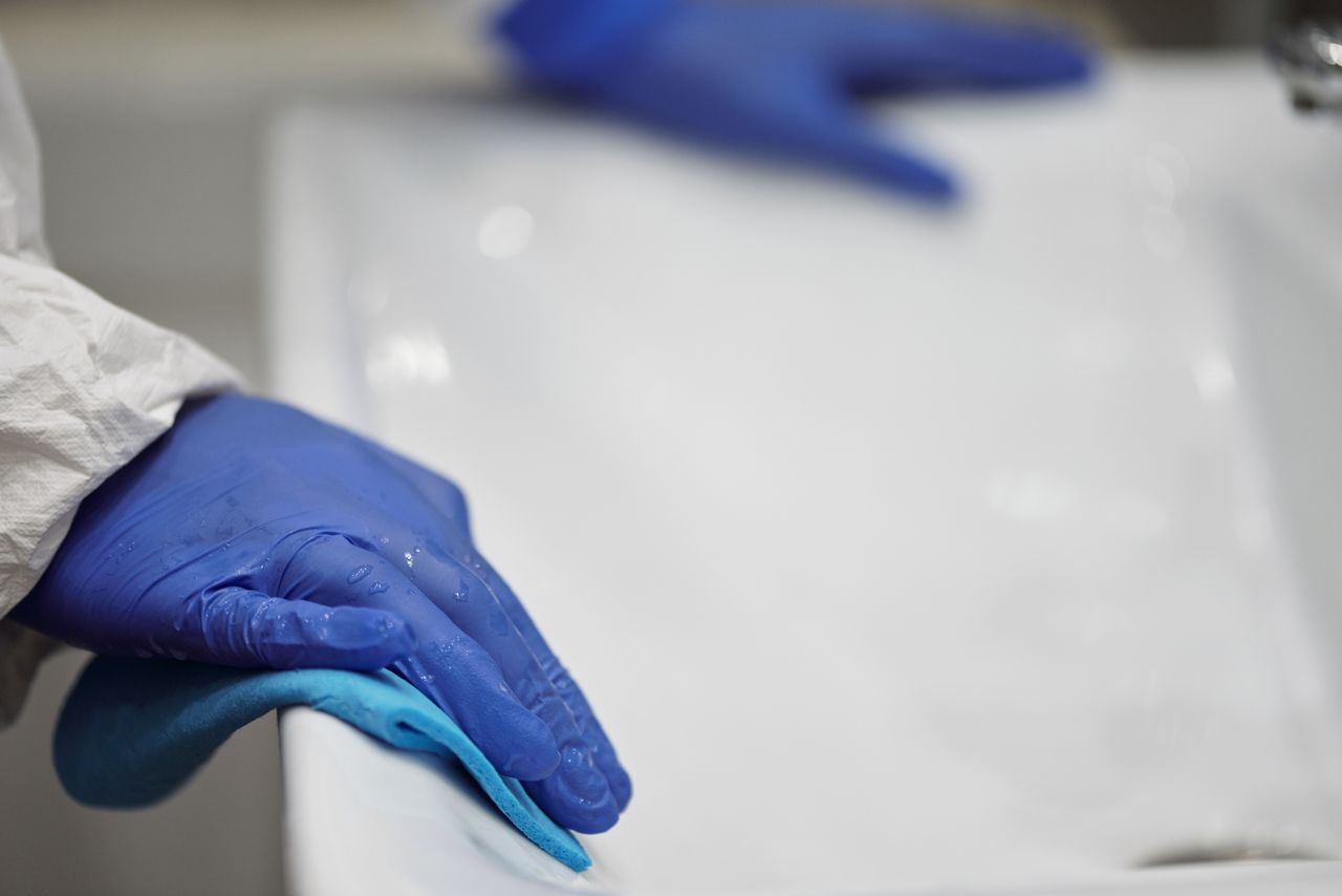 services-03 Vue rapprochée d’une personne désinfectant un lavabo de salle de bain avec des gants et un chiffon, en mettant l’accent sur l’hygiène et la propreté.
